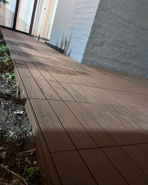 Deck WPC instalado junto a una pared de ladrillo blanco, fotografiado de noche
