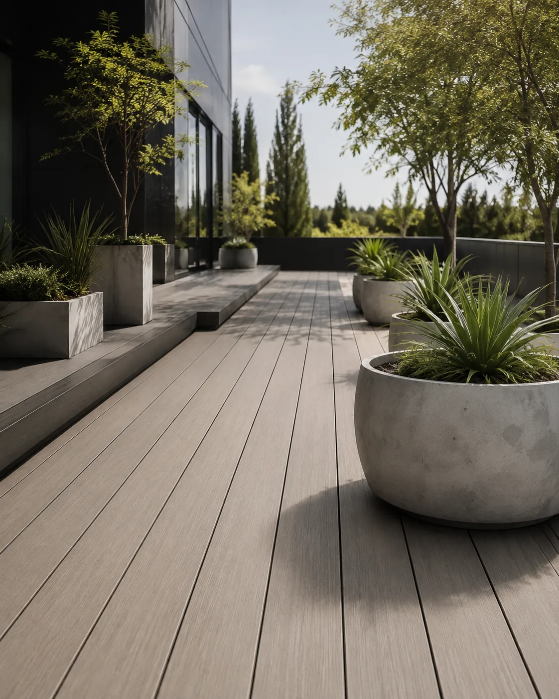 Deck exterior con macetones de hormigón y vegetación, frente a una fachada vidriada